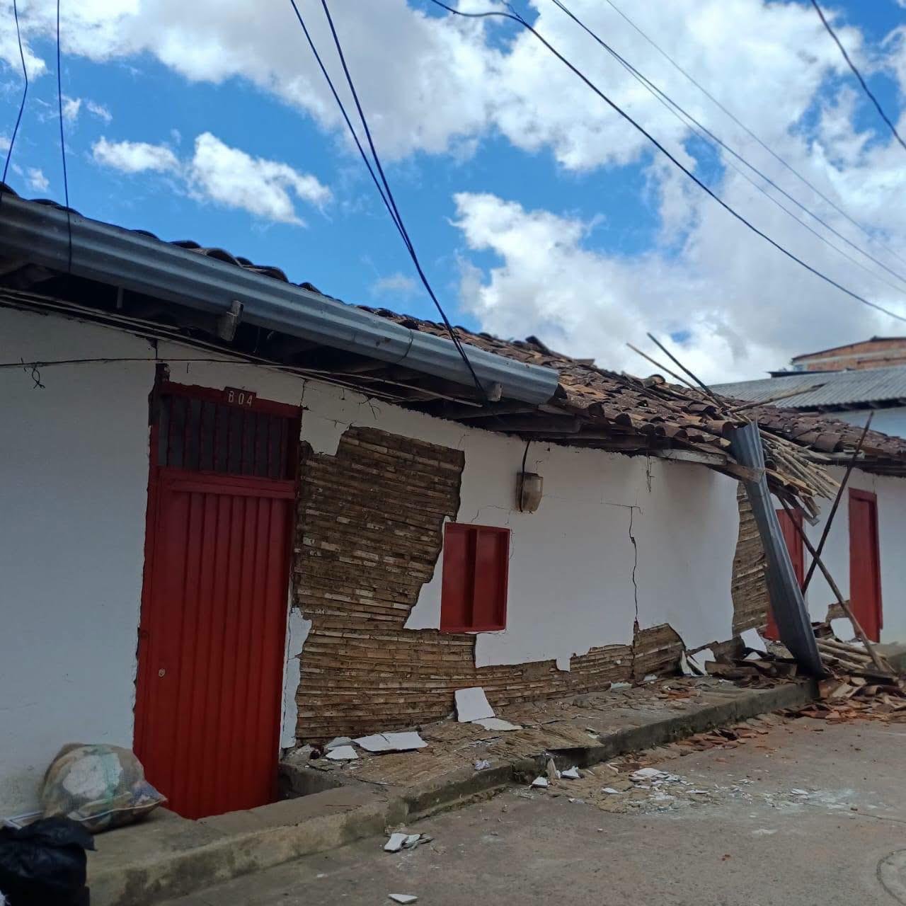 Fachada blanca con puertas rojas donde el revoque se desprendió y dejó a la vista la caña y el barro del muro